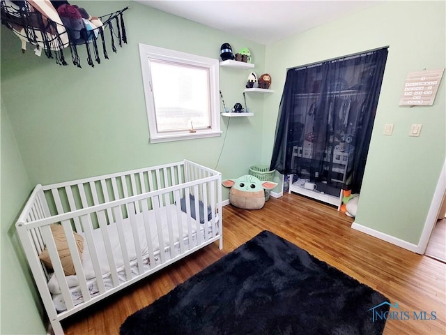 bedroom featuring wood-type flooring and a nursery area