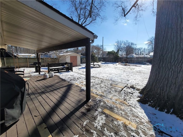 snow covered deck featuring area for grilling and a storage shed