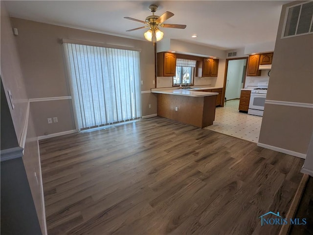 kitchen featuring a breakfast bar area, white range with gas stovetop, light wood-type flooring, kitchen peninsula, and ceiling fan