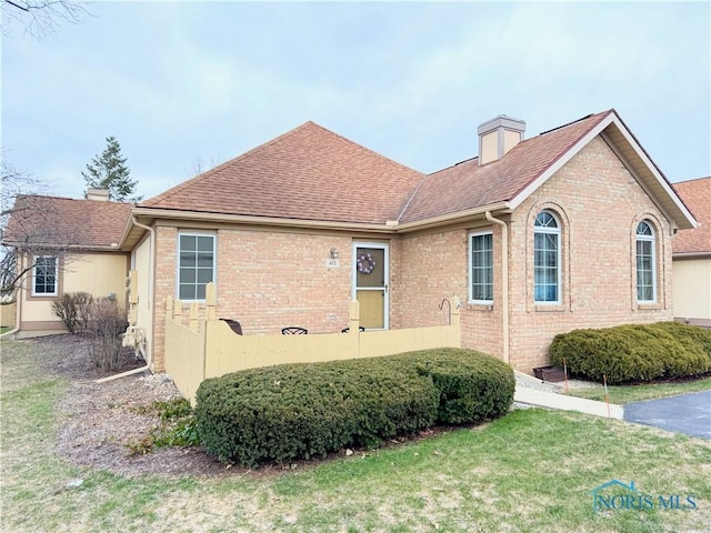 view of front of home with a front yard, roof with shingles, a chimney, and brick siding