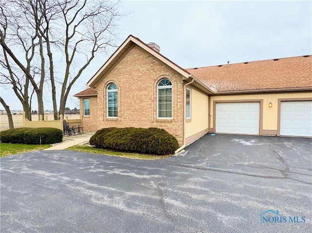 view of front of house featuring a garage, a chimney, aphalt driveway, and brick siding