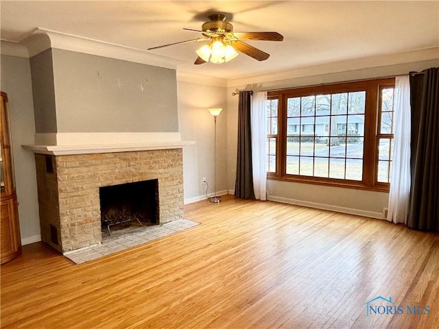 unfurnished living room featuring light wood finished floors, baseboards, crown molding, and a stone fireplace