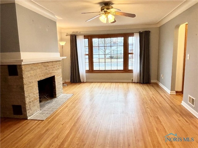 unfurnished living room with arched walkways, a tile fireplace, light wood-style flooring, visible vents, and baseboards