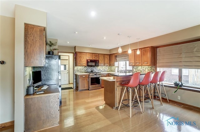 kitchen with pendant lighting, a kitchen bar, decorative backsplash, kitchen peninsula, and stainless steel range oven