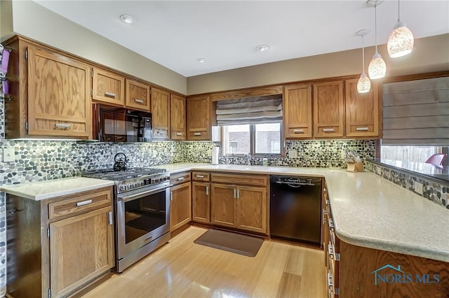 kitchen featuring sink, hanging light fixtures, tasteful backsplash, black appliances, and light wood-type flooring