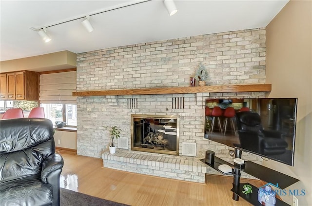 living room with rail lighting, a brick fireplace, and light hardwood / wood-style floors