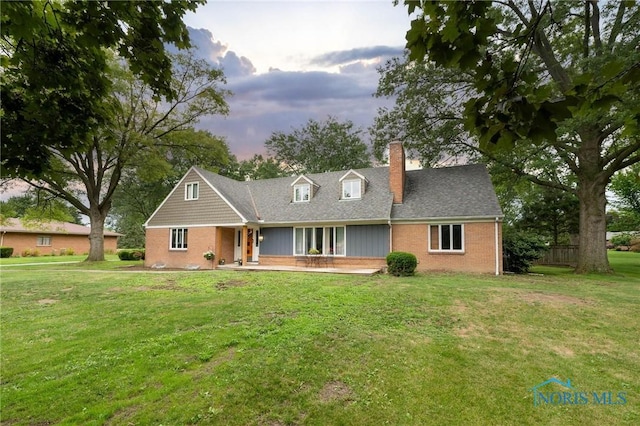 back house at dusk featuring a lawn