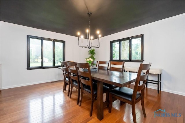 dining area with hardwood / wood-style flooring, ornamental molding, and an inviting chandelier