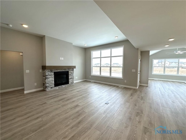 unfurnished living room featuring light hardwood / wood-style flooring, a stone fireplace, a wealth of natural light, and ceiling fan