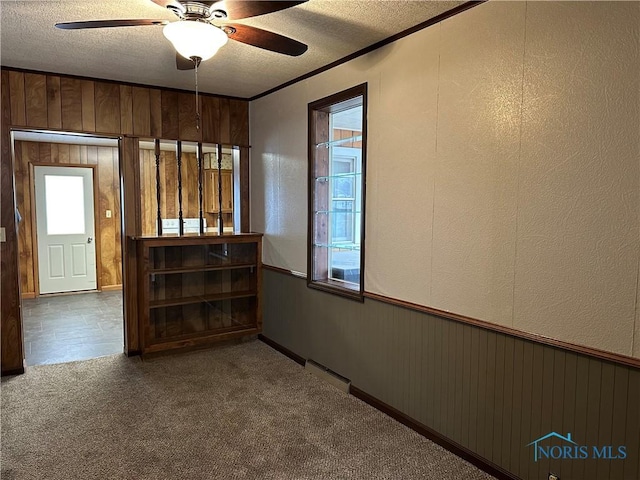 spare room featuring crown molding, carpet, a wealth of natural light, a textured ceiling, and wood walls