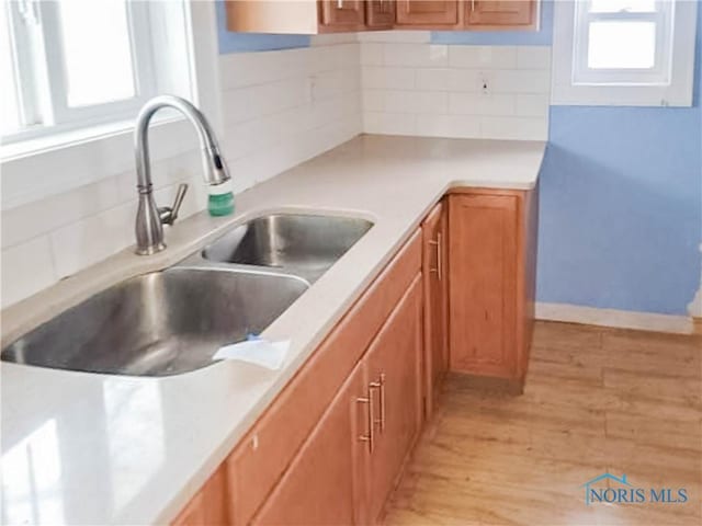 kitchen with decorative backsplash, a healthy amount of sunlight, sink, and light hardwood / wood-style flooring