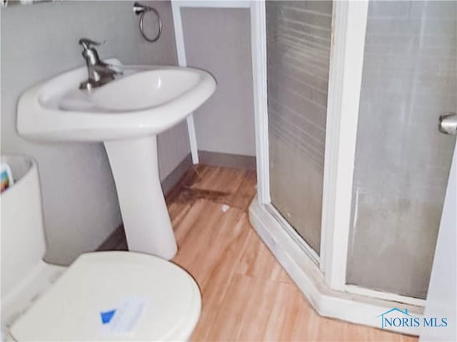 bathroom with wood-type flooring, a shower with door, and toilet