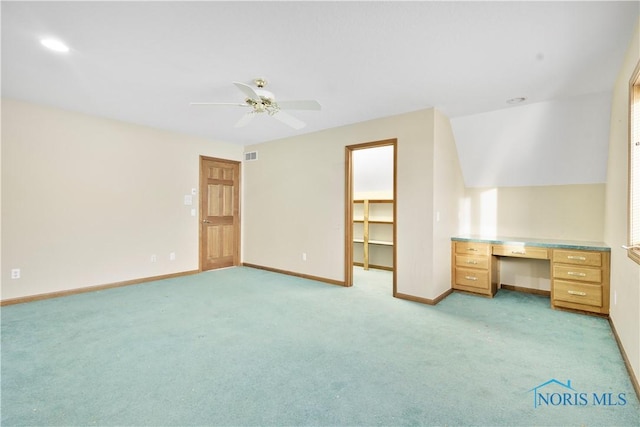 interior space featuring ceiling fan, a spacious closet, built in desk, and light carpet