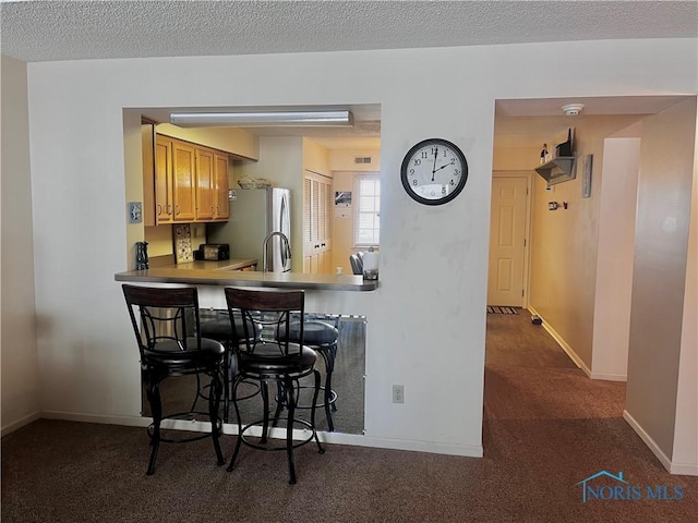 kitchen featuring carpet floors, a breakfast bar, a textured ceiling, and stainless steel refrigerator