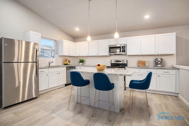 kitchen featuring appliances with stainless steel finishes, hanging light fixtures, light stone countertops, white cabinets, and a kitchen island