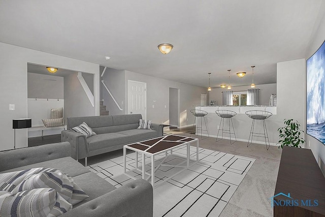 living room with stairway, baseboards, and light colored carpet