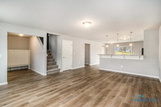 unfurnished living room featuring stairs, wood finished floors, and baseboards