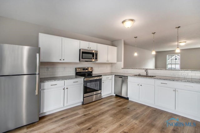 kitchen with sink, hanging light fixtures, kitchen peninsula, stainless steel appliances, and white cabinets