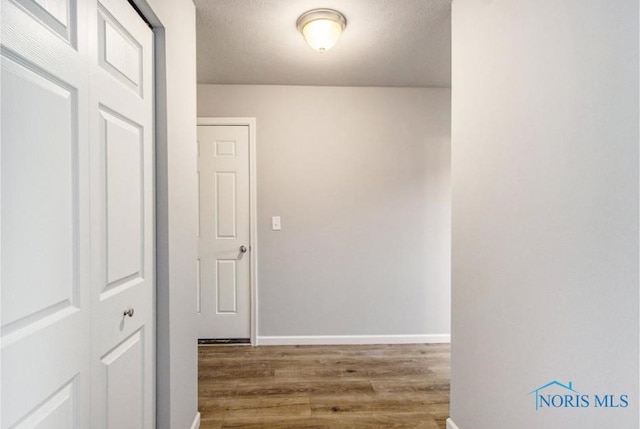 hall featuring baseboards, a textured ceiling, and wood finished floors
