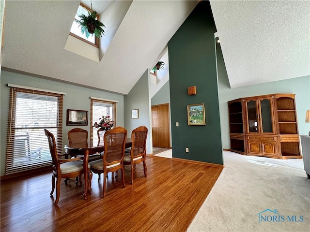 dining area featuring a skylight, wood-type flooring, high vaulted ceiling, and a textured ceiling