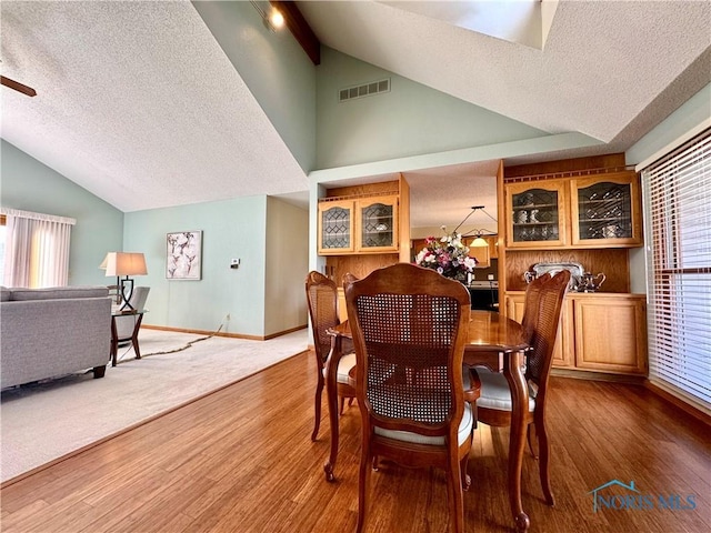 dining room featuring wood-type flooring, high vaulted ceiling, and a textured ceiling