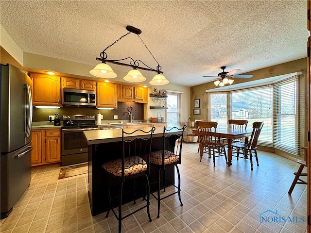 kitchen with appliances with stainless steel finishes, a breakfast bar, decorative light fixtures, decorative backsplash, and a center island