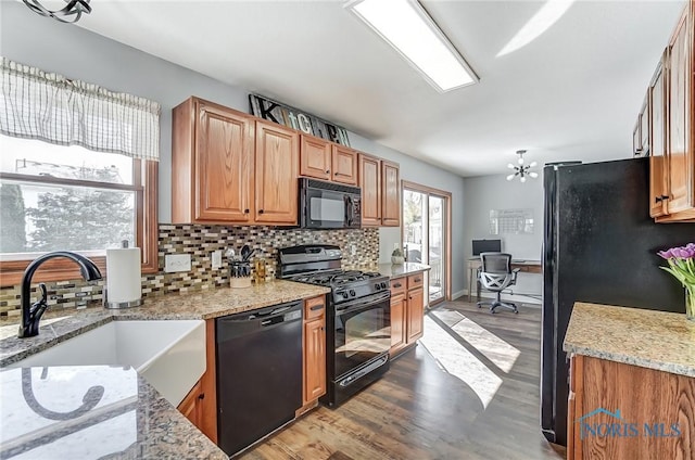 kitchen featuring light hardwood / wood-style flooring, light stone counters, black appliances, backsplash, and sink