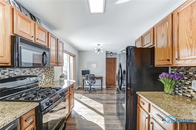 kitchen featuring tasteful backsplash, light stone countertops, black appliances, light hardwood / wood-style floors, and an inviting chandelier