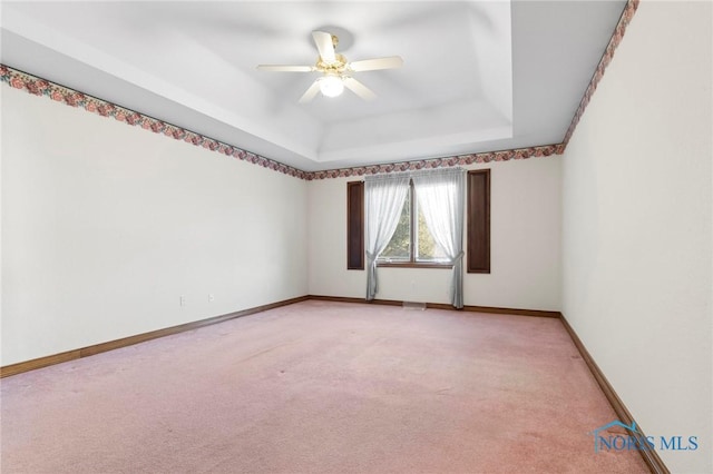 carpeted spare room with a raised ceiling and ceiling fan