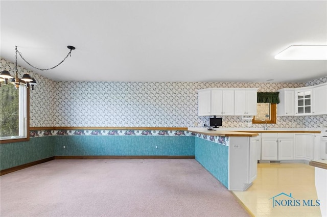 kitchen with white cabinetry, range, a chandelier, light carpet, and hanging light fixtures