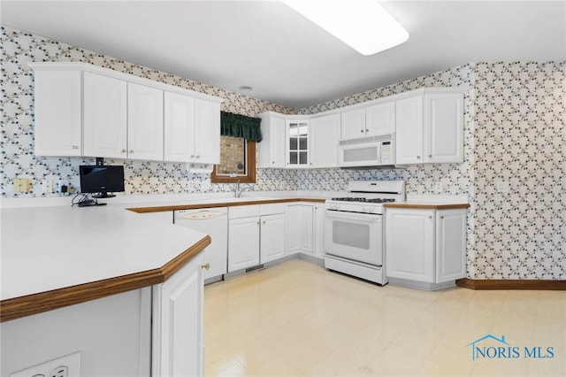 kitchen with sink, white appliances, kitchen peninsula, and white cabinets