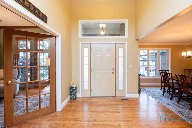 foyer with crown molding, a notable chandelier, and light wood-type flooring