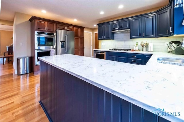 kitchen with sink, light hardwood / wood-style flooring, appliances with stainless steel finishes, beverage cooler, and decorative backsplash