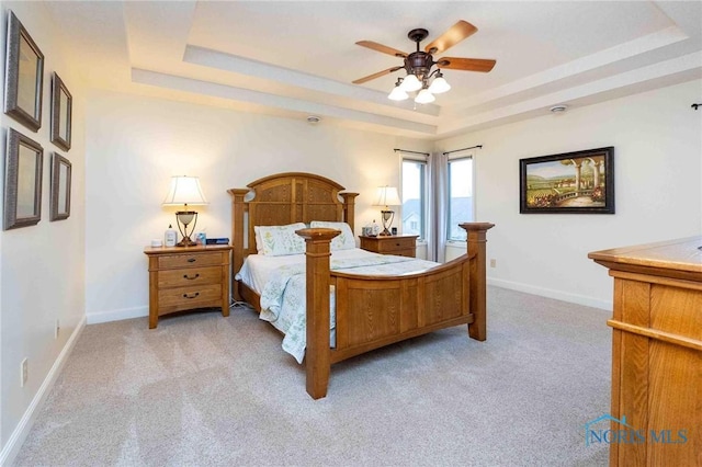 carpeted bedroom with ceiling fan and a tray ceiling