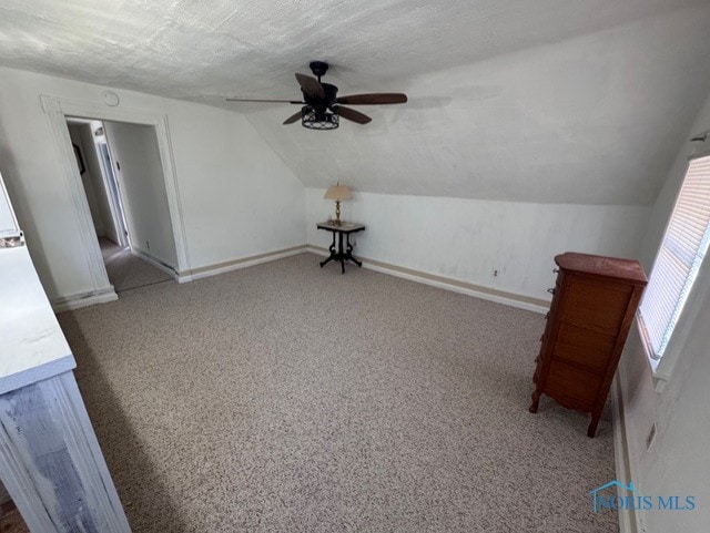 interior space featuring ceiling fan, vaulted ceiling, carpet, and a textured ceiling