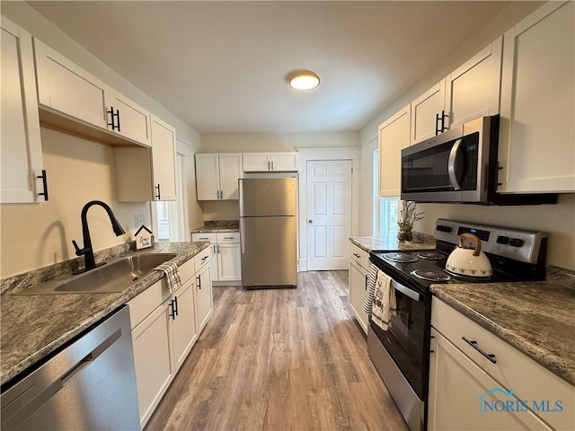 kitchen with white cabinets, appliances with stainless steel finishes, sink, and dark stone counters