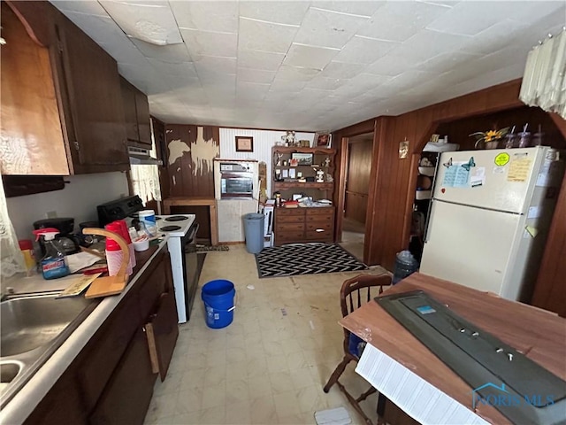 kitchen featuring white refrigerator, sink, electric range, and wood walls