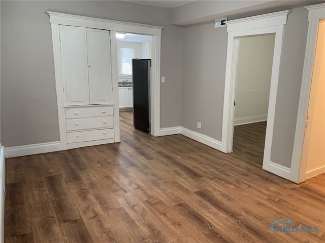 unfurnished bedroom featuring black refrigerator, a barn door, and dark wood-type flooring