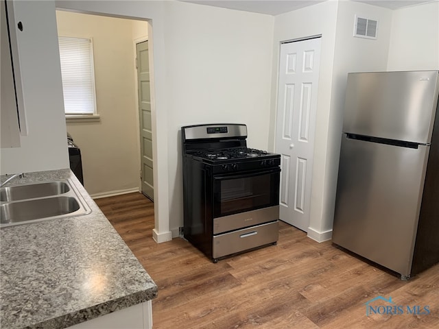 kitchen with stainless steel refrigerator, gas range oven, sink, and hardwood / wood-style flooring