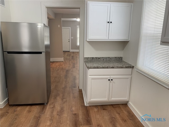 kitchen featuring dark stone countertops, dark hardwood / wood-style flooring, stainless steel fridge, and white cabinets