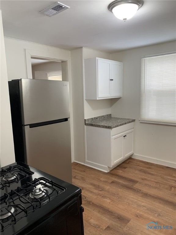 kitchen featuring black gas range, stainless steel fridge, white cabinets, and light wood-type flooring