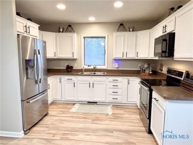 kitchen with stainless steel appliances, dark countertops, a sink, and white cabinets