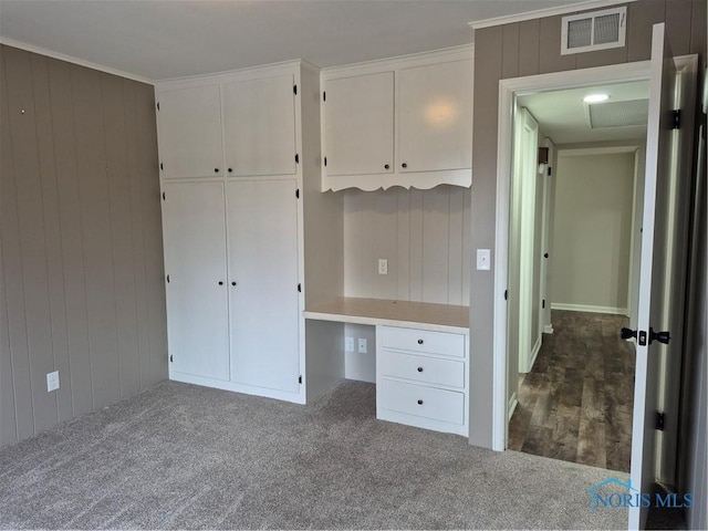 unfurnished bedroom featuring wooden walls, built in desk, and dark carpet