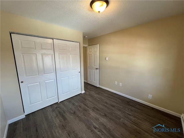 unfurnished bedroom with dark hardwood / wood-style flooring, a baseboard heating unit, a closet, and a textured ceiling