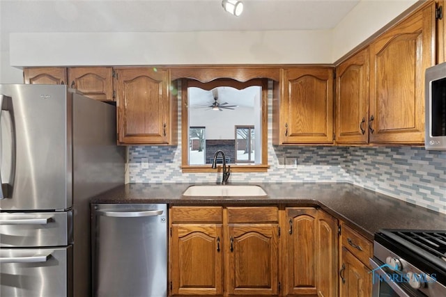 kitchen with stainless steel appliances, sink, backsplash, ceiling fan, and dark stone counters