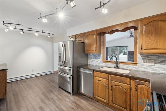 kitchen with light wood-type flooring, sink, a baseboard radiator, appliances with stainless steel finishes, and decorative backsplash