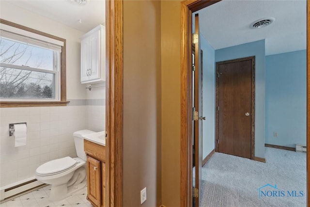 bathroom with a baseboard radiator, toilet, vanity, and tile walls