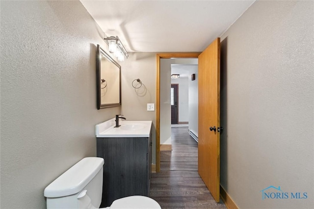 bathroom with vanity, toilet, wood finished floors, a textured wall, and baseboards