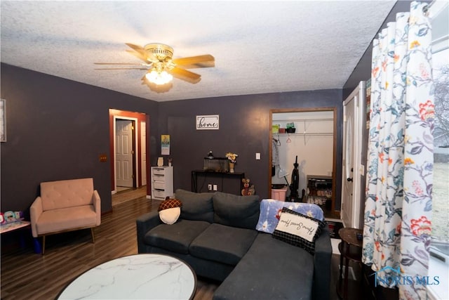 living room featuring ceiling fan, dark wood-type flooring, and a textured ceiling