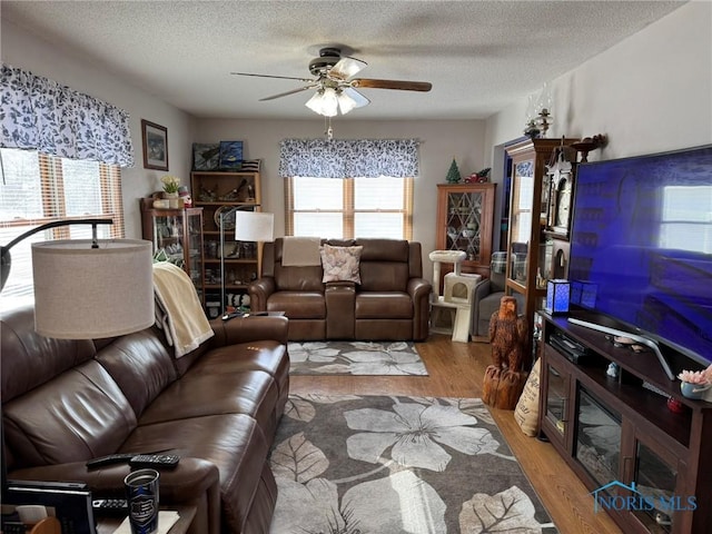 living room with ceiling fan, a textured ceiling, and light wood-type flooring